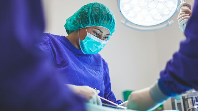 A female surgeon in a blue surgical robe and face mask.