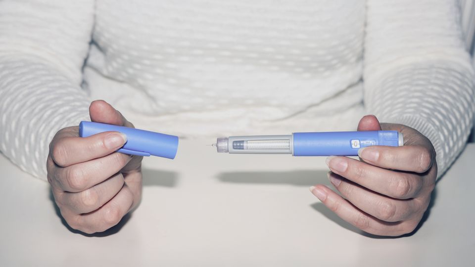 Person holding a GLP-1 injection pen used for managing type 2 diabetes and weight loss.