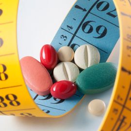 A selection of different drugs on top of a yellow tape measure used for measuring weight loss. 
