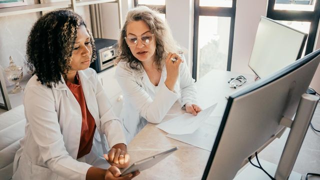 Two healthcare professionals in lab coats reviewing medical data on a tablet and desktop monitor