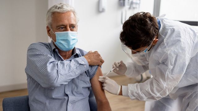 A man in a mask receiving a COVID-19 vaccination in his upper arm.