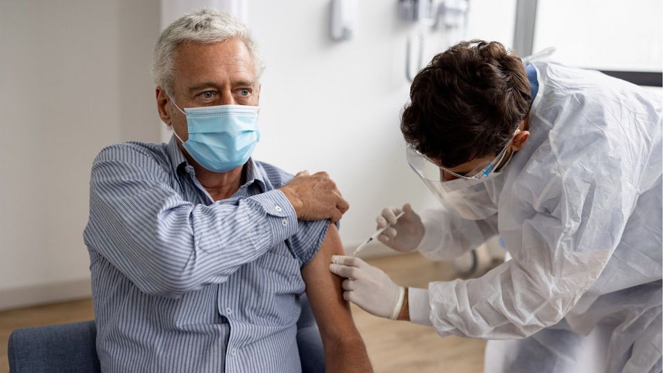 A man in a mask receiving a COVID-19 vaccination in his upper arm.