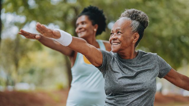Two older women smiling and exercising outdoors in an active, healthy lifestyle setting.