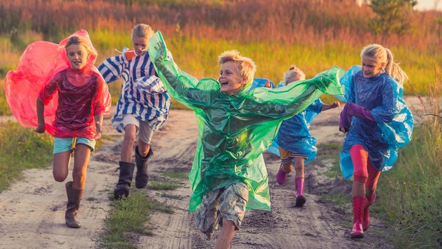 Children running joyfully outdoors in colorful rain ponchos, symbolizing diversity in autism subtypes.