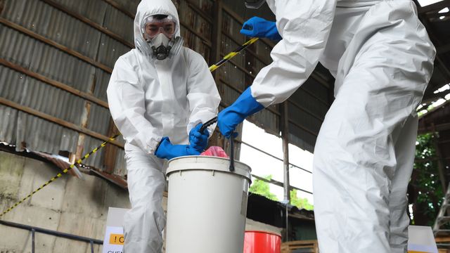 Two people in hazmat suits picking up a bucket containing unknown contaminants.