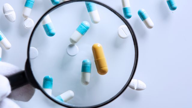 Magnifying glass highlighting a yellow capsule among assorted pills, symbolizing gabapentin.