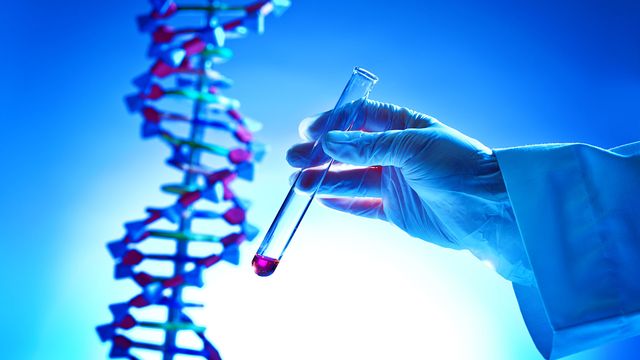 Gloved hand holding a test tube near a DNA double helix, symbolizing gene therapy research.