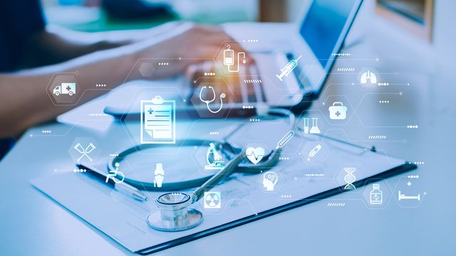 A person typing on a laptop, patient notes and a stethoscope alongside, overlaid with graphics representing multimodal patient data.
