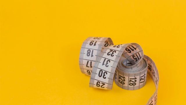 A white tape measure used for measuring weight loss against a yellow background.