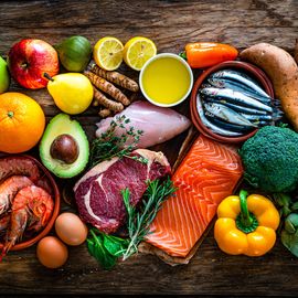 Selection of healthy foods on a wooden table, including fruits, vegetables, nuts and fish. 