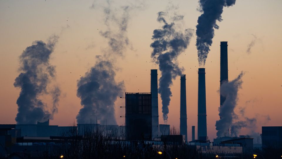 Industrial smokestacks emitting thick plumes of smoke into the air at sunset, symbolizing pollution.