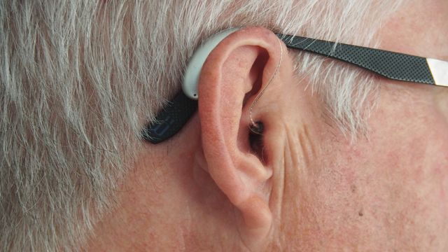 Close-up of an older adult wearing a hearing aid behind the ear.