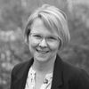 A black and white image of Dr. Trainer, a white woman with glasses and a blonde bob haircut, smiling at the camera.