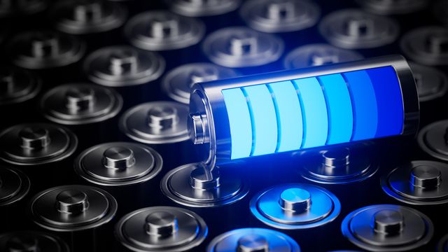 Close-up of a glowing blue battery icon resting on metallic cylindrical cells, symbolizing advanced battery technologies. 