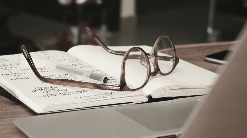 Glasses on a notebook. Laptop and pen visible.