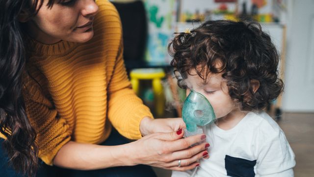 A mother helping her young child use an inhalation device to receive cystic fibrosis treatment.