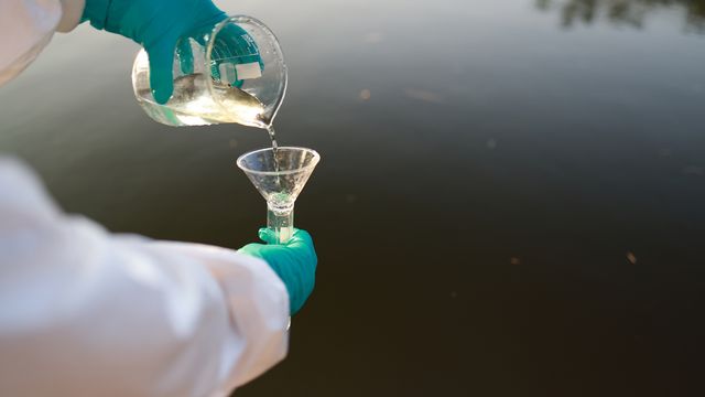 Scientist pouring water from a beaker into a test tube whilst overlooking water 