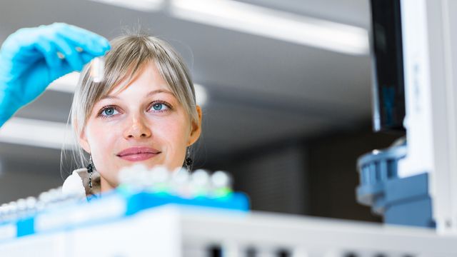 Female scientist examining a vial in a laboratory, highlighting focus on scientific research.