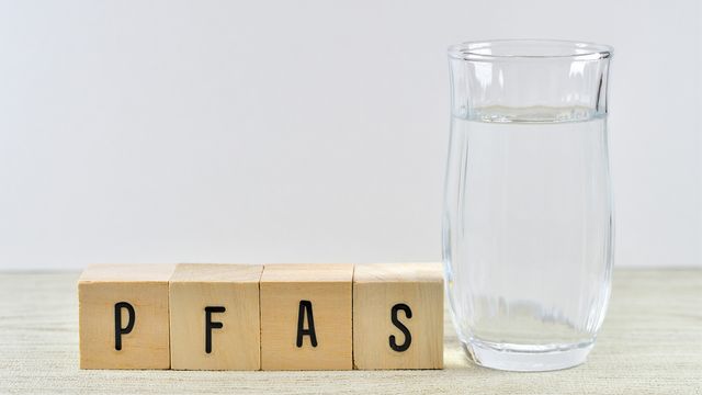 Wooden blocks spelling 'PFAS' next to a glass of water, symbolizing concerns about per- and polyfluoroalkyl substances in drinking water