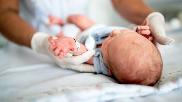 Newborn baby lying on a blanket being examined by a healthcare professional.