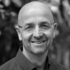 Smiling bald man in glasses posing outdoors for a professional researcher headshot.