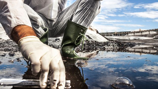 Scientist in protective gear collecting wastewater samples from a polluted site for analysis.