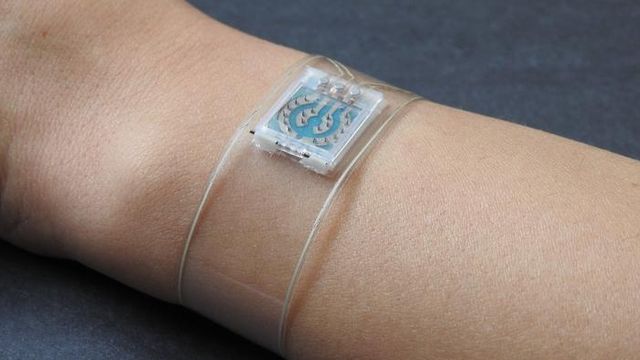 A transparent strip of plastic wrapped around a wrist, a white and blue microchip-like object in its centre.