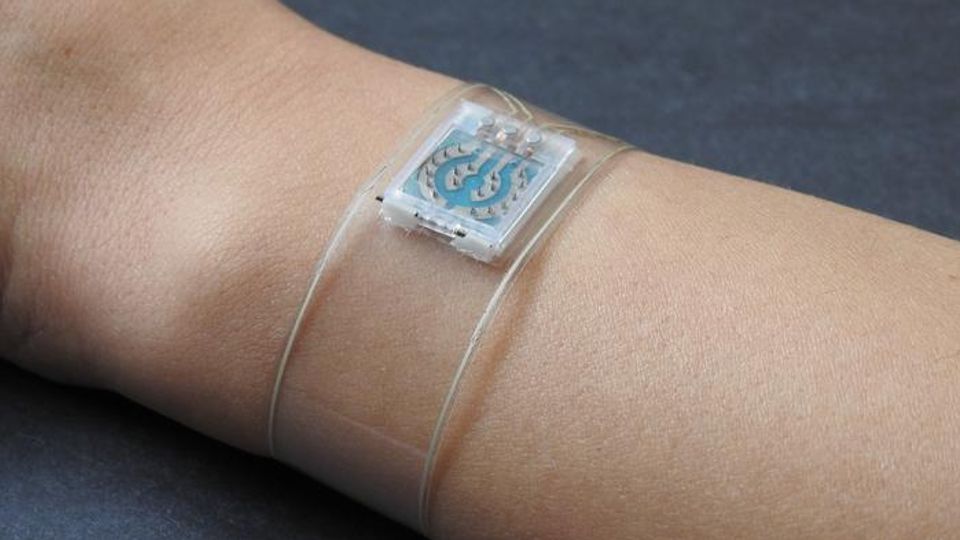 A transparent strip of plastic wrapped around a wrist, a white and blue microchip-like object in its centre.