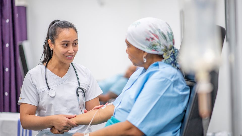 A doctor talking to a cancer patient while they receive cancer therapy via an IV drip.