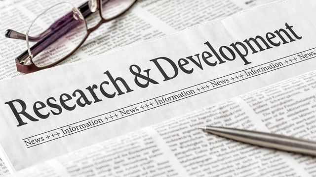 A pair of glasses and ball point pen laying on top of a folded newspaper with the headline "Research & Development".
